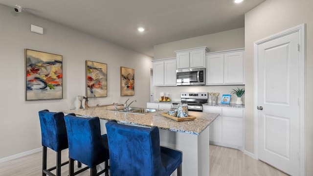 kitchen featuring a sink, a kitchen bar, light wood-style flooring, appliances with stainless steel finishes, and white cabinetry