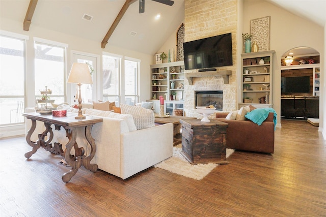 living area featuring beamed ceiling, a ceiling fan, wood finished floors, a stone fireplace, and high vaulted ceiling