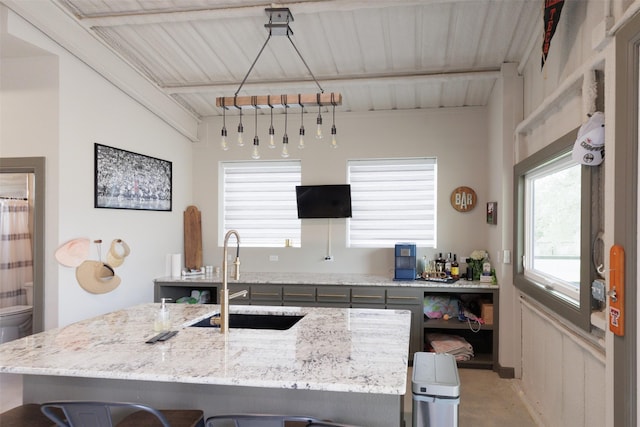 kitchen with a kitchen island with sink, a kitchen breakfast bar, a sink, beamed ceiling, and light stone countertops