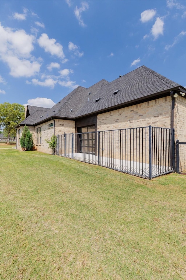 back of property featuring fence, roof with shingles, a yard, and brick siding