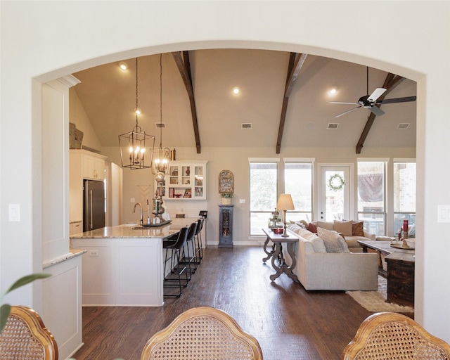 living area with arched walkways, dark wood-style flooring, vaulted ceiling with beams, and ceiling fan with notable chandelier