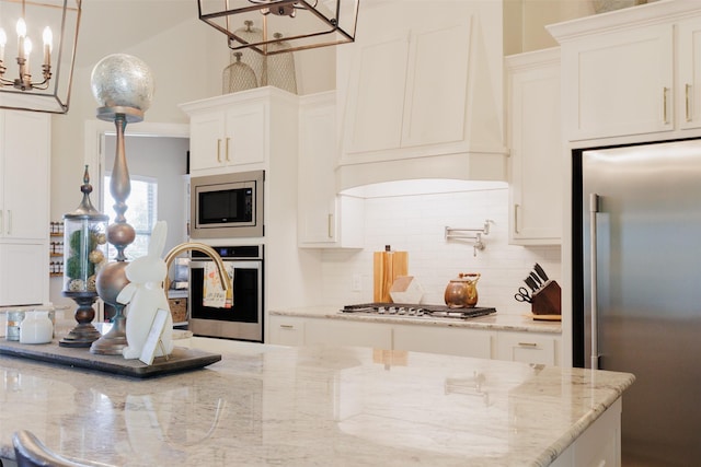 kitchen featuring white cabinets, stainless steel appliances, an inviting chandelier, light stone countertops, and tasteful backsplash