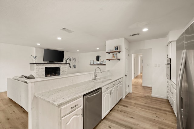 1764 Brown Trl, Hurst, TX 76054 - kitchen featuring a peninsula, appliances with stainless steel finishes, a sink, light wood-style floors, and light stone countertops