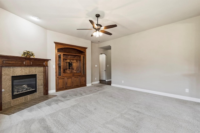 unfurnished living room with ceiling fan, arched walkways, carpet floors, a tile fireplace, and baseboards