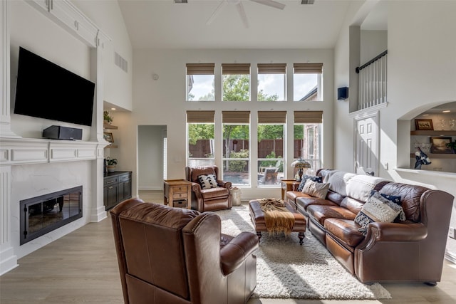 living room with arched walkways, a high ceiling, a ceiling fan, and a premium fireplace