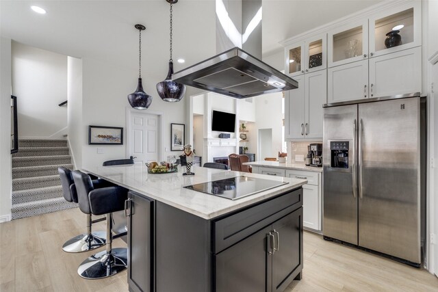 kitchen with light stone counters, island range hood, black electric stovetop, a kitchen bar, and stainless steel refrigerator with ice dispenser