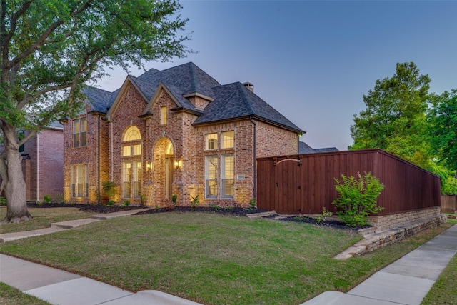 french country style house featuring fence, a shingled roof, brick siding, and a front yard