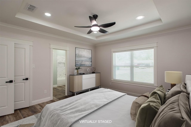 bedroom with visible vents, baseboards, wood finished floors, and a tray ceiling