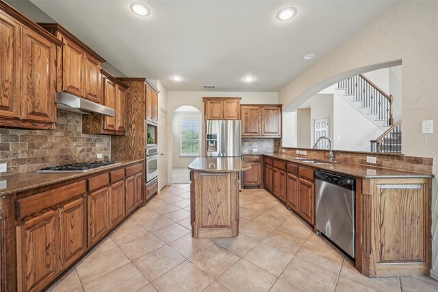 kitchen with stainless steel appliances, arched walkways, under cabinet range hood, and a sink