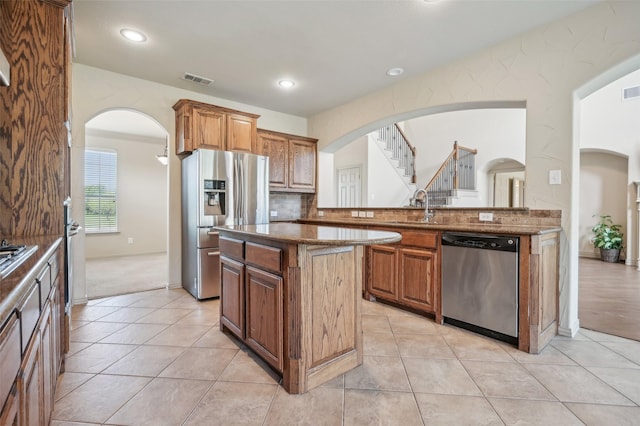 kitchen with arched walkways, a center island, dark stone counters, and stainless steel appliances