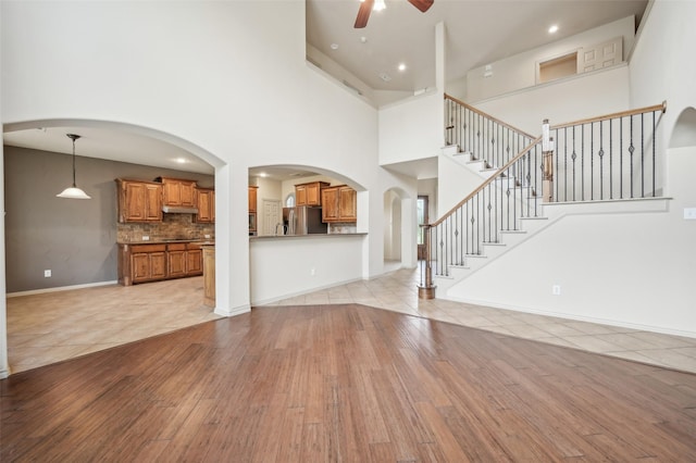 unfurnished living room with stairway, ceiling fan, light wood finished floors, baseboards, and a high ceiling