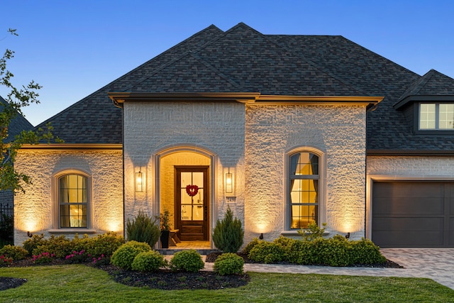 french country style house with roof with shingles, a front lawn, driveway, a garage, and brick siding