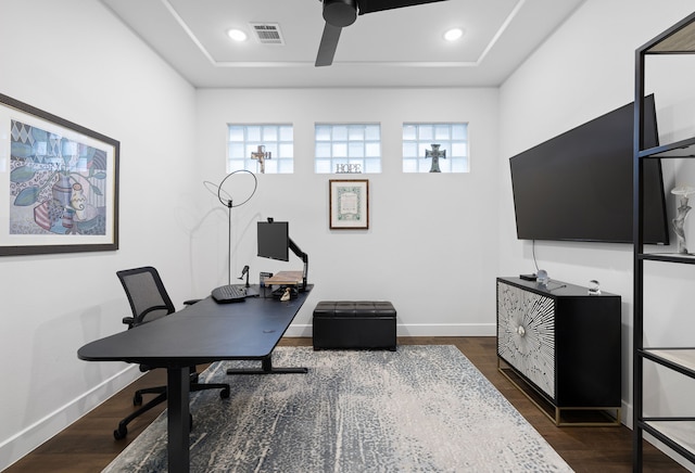 home office featuring dark wood-style floors, a tray ceiling, baseboards, visible vents, and ceiling fan