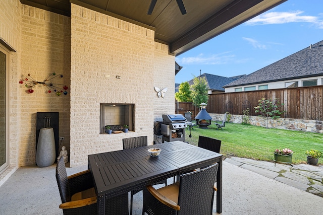 view of patio featuring a ceiling fan, outdoor dining space, grilling area, fence private yard, and an outdoor brick fireplace
