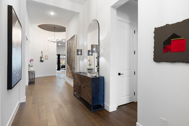 corridor featuring baseboards, wood finished floors, recessed lighting, and a notable chandelier