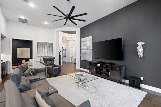 living area featuring arched walkways, dark wood-style flooring, baseboards, visible vents, and ceiling fan with notable chandelier