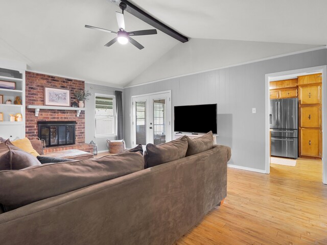 living area with lofted ceiling with beams, a brick fireplace, ceiling fan, light wood-type flooring, and baseboards