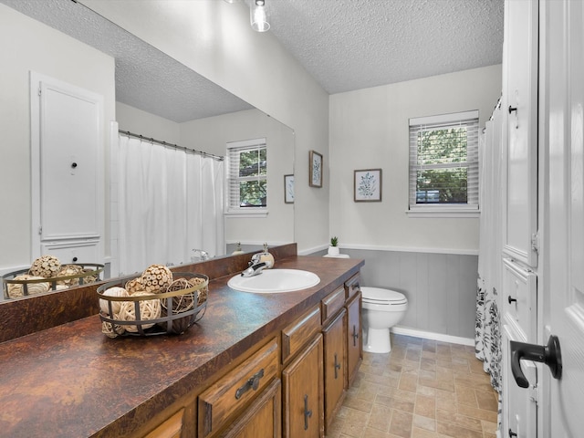 full bathroom with a wainscoted wall, a healthy amount of sunlight, a textured ceiling, and vanity