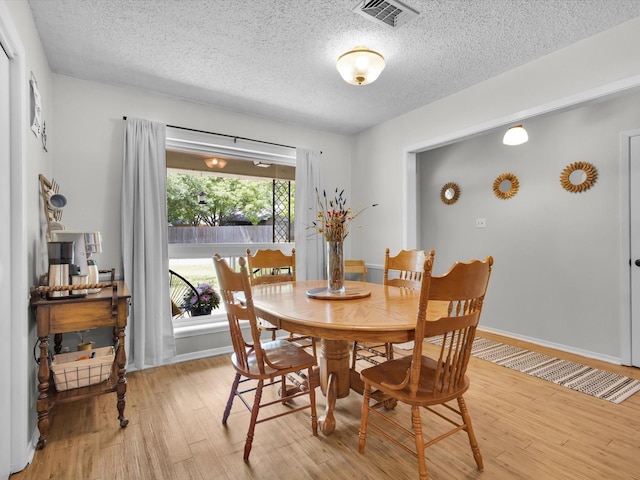 dining area with light wood finished floors, a textured ceiling, visible vents, and baseboards