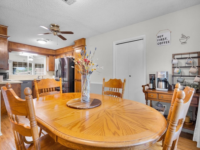 dining area with a ceiling fan, light wood-style floors, and a textured ceiling