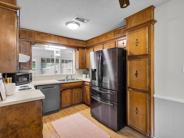 kitchen featuring brown cabinetry, appliances with stainless steel finishes, light countertops, a sink, and visible vents