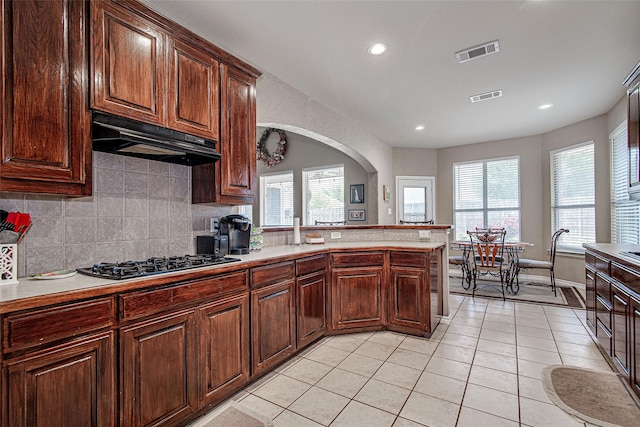 kitchen with gas cooktop, under cabinet range hood, visible vents, and arched walkways
