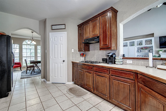 kitchen featuring under cabinet range hood, light countertops, light tile patterned floors, arched walkways, and freestanding refrigerator