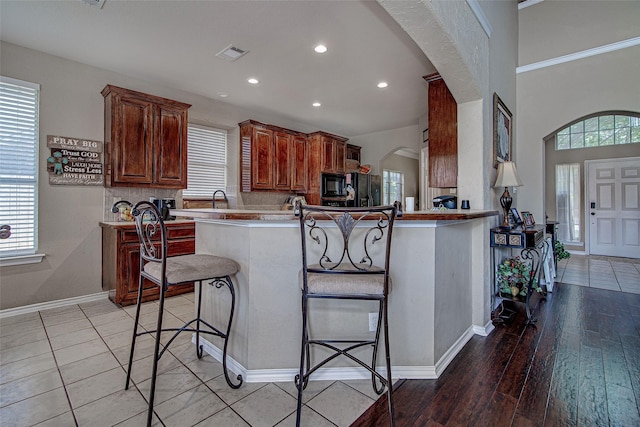 kitchen with black appliances, a breakfast bar area, arched walkways, visible vents, and recessed lighting