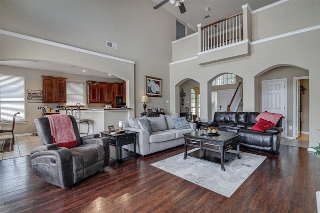 living room featuring a ceiling fan, stairs, arched walkways, baseboards, and visible vents