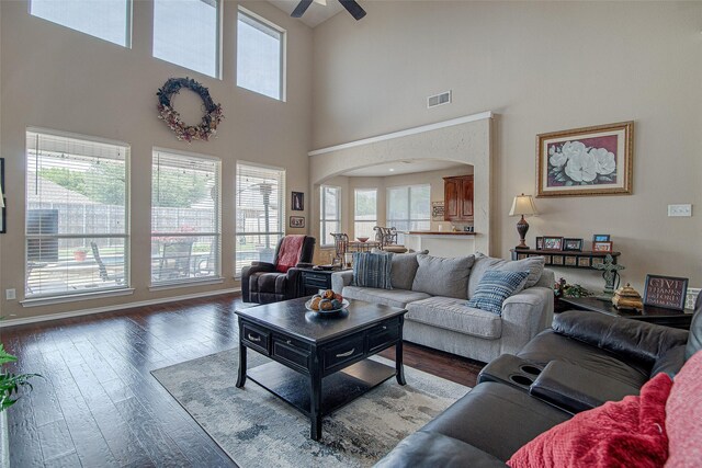 living area featuring arched walkways, visible vents, a high ceiling, ceiling fan, and wood-type flooring