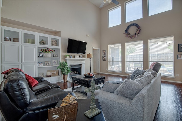 living area with dark wood-style flooring, baseboards, a high ceiling, ceiling fan, and a fireplace