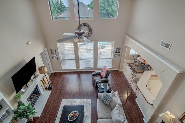 living area with baseboards, a towering ceiling, a ceiling fan, wood finished floors, and a fireplace