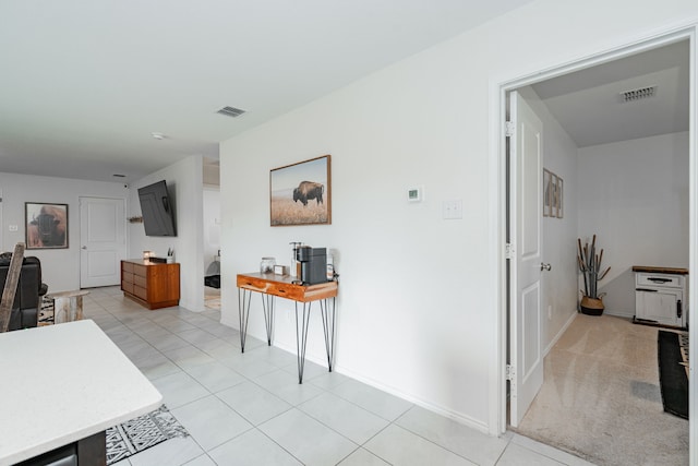 corridor featuring baseboards, visible vents, and light tile patterned floors