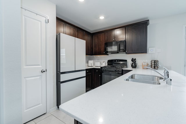 kitchen featuring light tile patterned floors, a sink, dark brown cabinetry, black appliances, and a peninsula