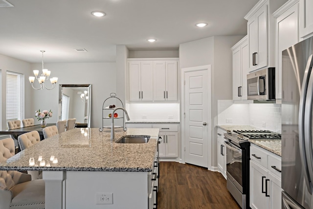 kitchen featuring a sink, dark wood-style flooring, a notable chandelier, a kitchen bar, and appliances with stainless steel finishes