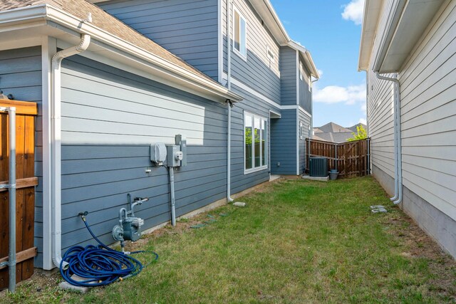 view of property exterior with central air condition unit, fence, roof with shingles, and a lawn