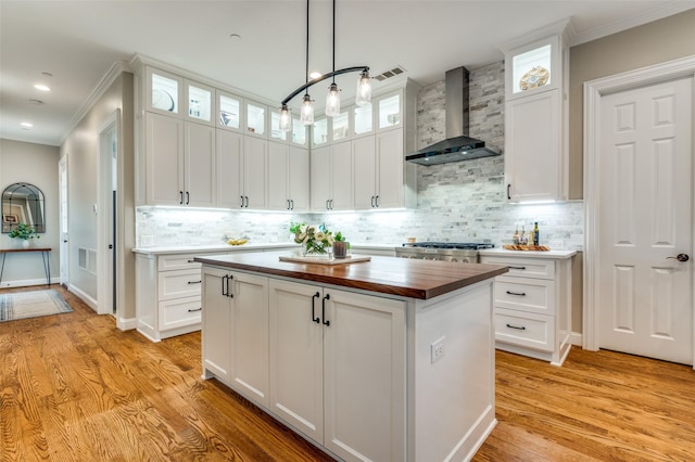 kitchen featuring white cabinets, a center island, tasteful backsplash, wall chimney range hood, and wooden counters