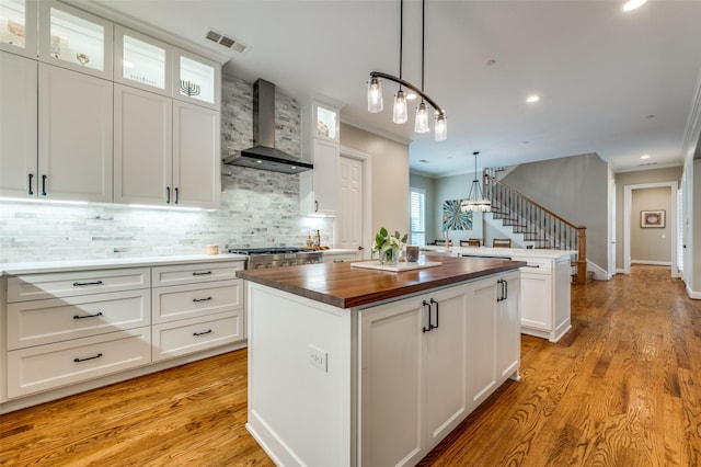 kitchen featuring wall chimney range hood, crown molding, wood counters, visible vents, and a kitchen island
