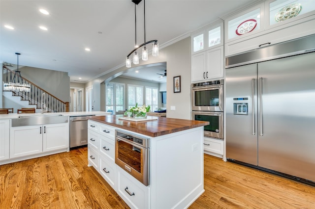 kitchen with light wood finished floors, stainless steel appliances, a sink, glass insert cabinets, and butcher block counters