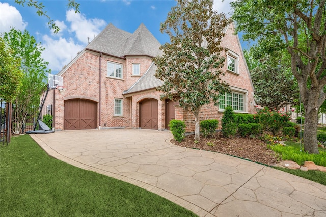 french provincial home featuring driveway, brick siding, a front yard, and a garage