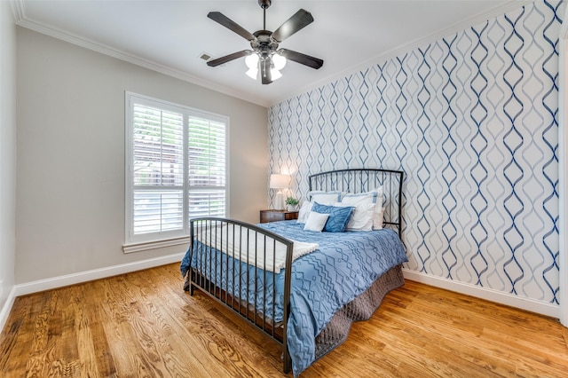 bedroom featuring light wood finished floors, baseboards, visible vents, ceiling fan, and crown molding