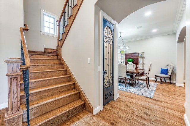 stairway with arched walkways, baseboards, an inviting chandelier, wood finished floors, and ornamental molding