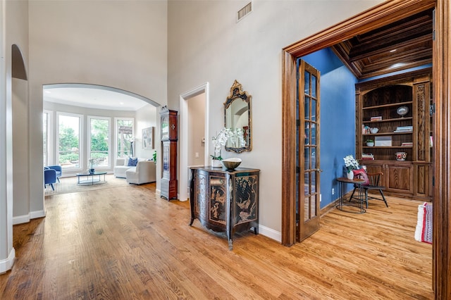 hall featuring arched walkways, wood finished floors, visible vents, and crown molding