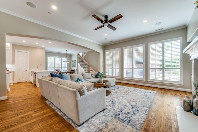 living area with visible vents, a ceiling fan, ornamental molding, arched walkways, and stairs