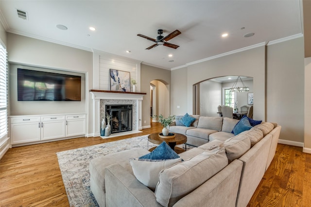 living room with light wood-style flooring, arched walkways, visible vents, ceiling fan with notable chandelier, and ornamental molding