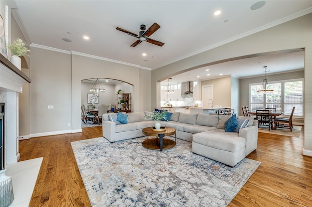 living room featuring light wood-style flooring, arched walkways, recessed lighting, ceiling fan with notable chandelier, and ornamental molding