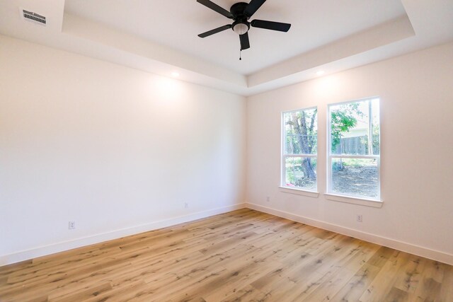 empty room featuring light wood-style flooring, a raised ceiling, baseboards, visible vents, and recessed lighting
