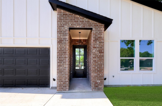 entrance to property with board and batten siding, an attached garage, driveway, and brick siding
