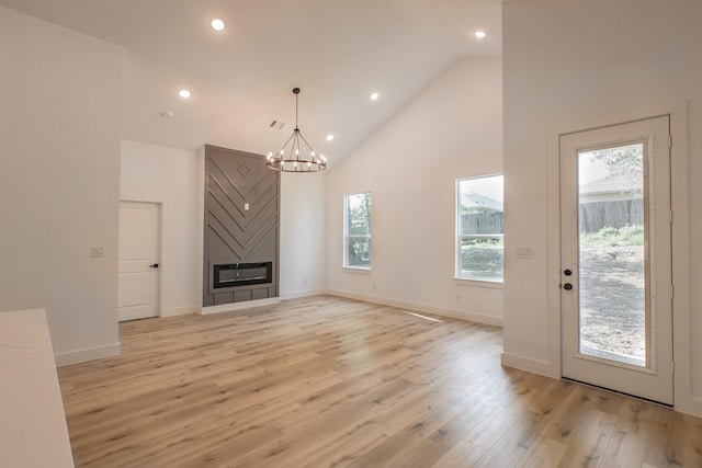 unfurnished living room featuring baseboards, recessed lighting, light wood-style floors, a notable chandelier, and high vaulted ceiling