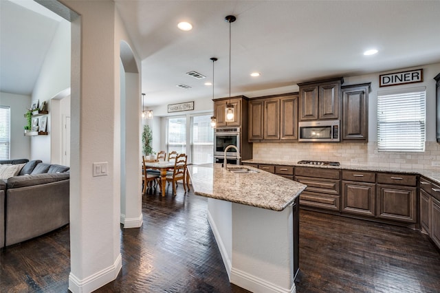 kitchen featuring light stone counters, a sink, arched walkways, tasteful backsplash, and appliances with stainless steel finishes